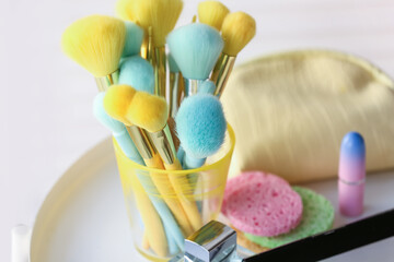 Holder with colorful makeup brushes on table in room, closeup