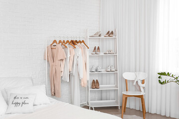 Interior of light bedroom with stylish clothes and shoes