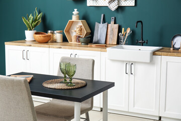 Dining table and white counters with kitchen utensils near green wall
