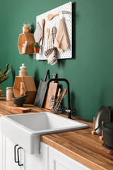 Cutting boards with kitchen utensils and sink on counters near green wall