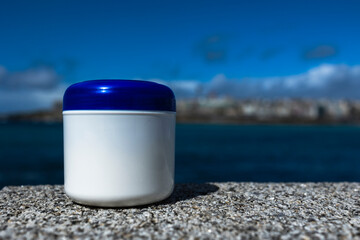A white jar of cream with a lid on the background of the ocean. Close-up.