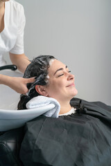 the cosmetologist washes the girl's head with shampoo for further procedures. black hair. plus size.