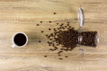 A glass jar filled with roasted coffee beans, which fell on the table, causing the coffee beans to...