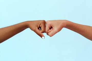 Black African American woman and white Caucasian woman punching on a blue background. Partnership and cooperation agreement, multiracial diversity and immigration concept. Stop racism.