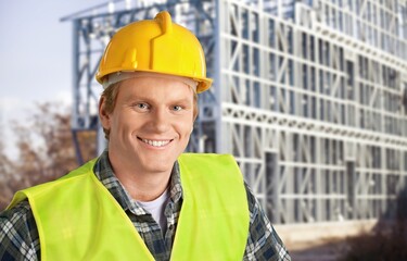 Young engineer handsome man or architect with safety helmet in construction site. Standing at modern building construction.