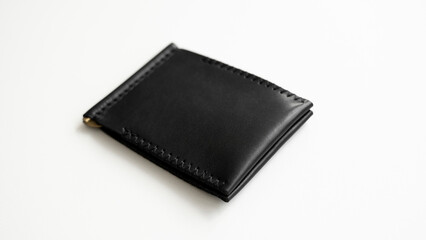 Empty black men's money clip handmade leather wallet with a two pockets for cards lies on a white table. Selective focus, copy space, close up.