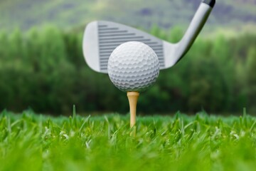 Golf club and ball on green grass ready to be struck on golf course background, evening time.
