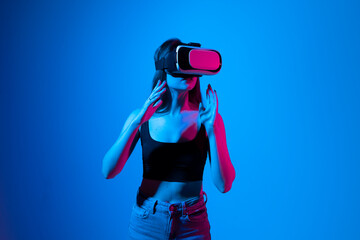 Young woman working in VR goggles on a grey background. Modern architect using virtual reality glasses at workplace. Designer working in augmented reality vr studio.