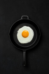 Fried egg in old black skillet. Dark background.