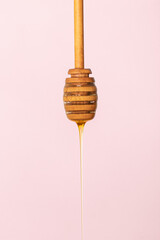 Honey dripping on wood honey catcher. in pink background.