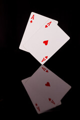 two red playing aces on a black background with reflection at the bottom