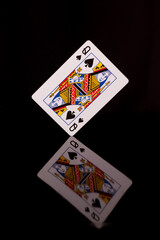 Playing card, queen of spades on a black background with reflection