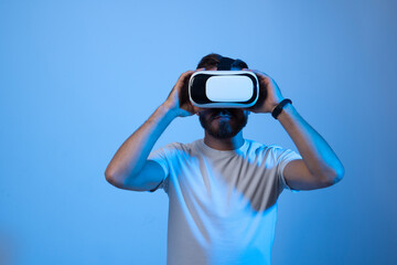 Young bearded man in virtual reality helmet plays online game in metaverse. Game simulates behavior in fictional world, gadgets and virtual reality addiction. Future technology concept.