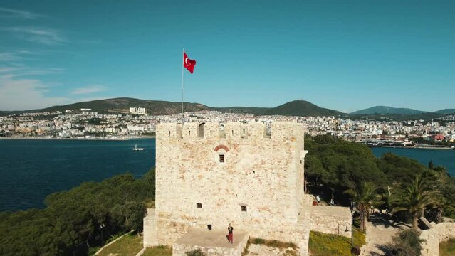 rone flight over the castle tower of Pigeon Island - Guvercinada in Kusadasi Turkey, summer sunny day, .turkish flag, big white cruiser in the port of Kusadasi