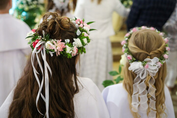 Dziewczynki stojące w kościele podczas uroczystości pierwszej komunii świętej z wiankami kwiatów na głowach - obrazy, fototapety, plakaty