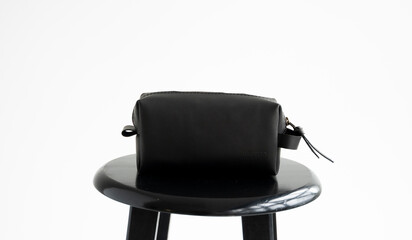 Man's black leather personal cosmetic bag or pouch for toiletry accessory on a black surface with white background. Style, retro, fashion, vintage and elegance.
