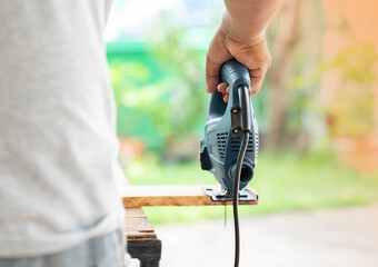 A carpenter uses an electric jigsaw to cut the wood on the table.