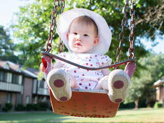 Caucasian baby girl sitting in a swing on a sunny summer day