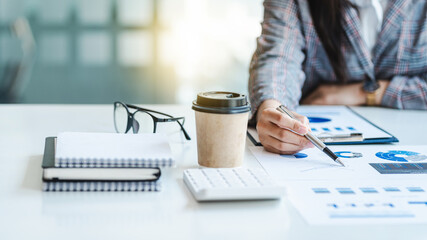 Close-up hands of businesswoman or female financial worker analysing financial data report, pointing pen on paperwork.