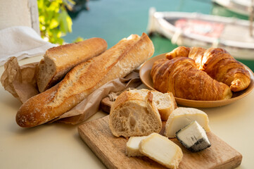Sunny morning in Provence, breakfast with fresh baked croissants, baquett bread, crottin goat cheese and view on fisherman's boats in harbour of Cassis, Provence, France