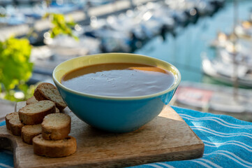 Homemade fish soup with croutons served with view on colorful fisherman's boats in harbour of Cassis, Privence, France.