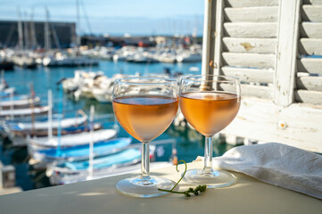 Cold rose wine in glasses served on outdoor terrace in sunlights with view on old fisherman's harbour with colourful boats in Cassis, Provence, France