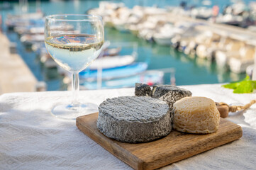 French goat cheeses crottin and selles-sur-cher served with view on boats in harbor of Cassis, Provence, France with glass of dry white wine