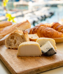 Sunny morning in Provence, breakfast with fresh baked croissants, baquett bread, crottin goat cheese and view on fisherman's boats in harbour of Cassis, Provence, France