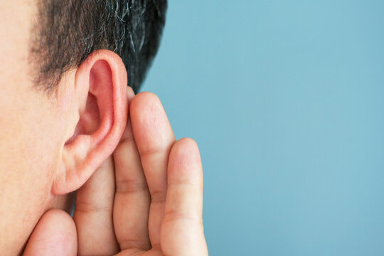 The man listens attentively with her palm to her ear, news concept.