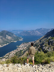 Fototapeta na wymiar Man is standing and looking at Kotor bay from above in Kotor, Montenegro