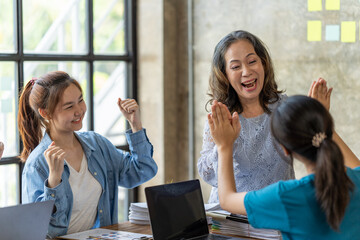 Diverse group of smiling young business people celebrating success with high fives while working together in a modern office, colleagues celebrate shared business success or victory in office.