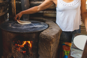 Mujer mexicana torteando maza de ma&iacute;z en un metate y una estufa de le&ntilde;a para hacer tortillas caseras  