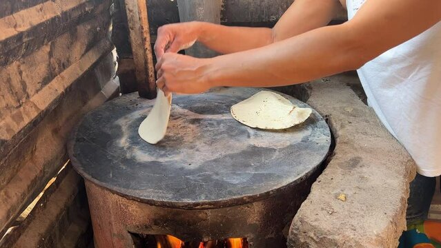 Mujer mexicana torteando maza de ma&iacute;z en un metate y una estufa de le&ntilde;a para hacer tortillas caseras  