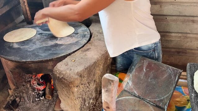 Mujer mexicana torteando maza de ma&iacute;z en un metate y una estufa de le&ntilde;a para hacer tortillas caseras  