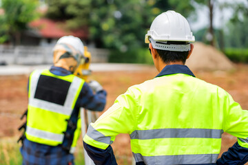 Asian engineers use yellow theodolite to find blueprints at building construction sites.