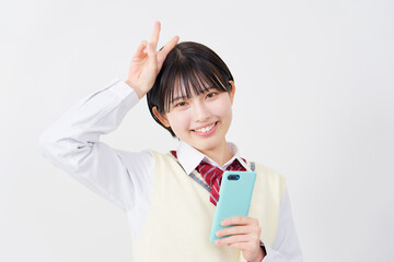 白背景でスマホを持ってピースサインする女子高生