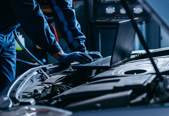 Close up hands of auto electrician using a computer laptop to diagnosing and checking up on car...