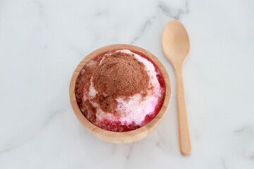 crushed ice Or shaved ice with sweet red water and sweetened condensed milk, Topped with chocolate powder, looks like a volcano. in a round wooden bowl with wooden spoon. It is a dessert.