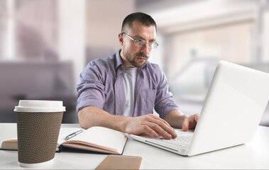 Fototapeta na wymiar Young smiling man in glasses using laptop sitting at home desk, watching webinar studying online,