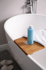 Bottle of bubble bath with foam and towel on tub in bathroom