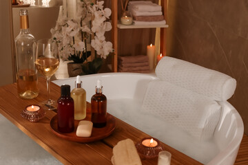 Fototapeta na wymiar Tub with soft bath pillow, toiletries and wine indoors