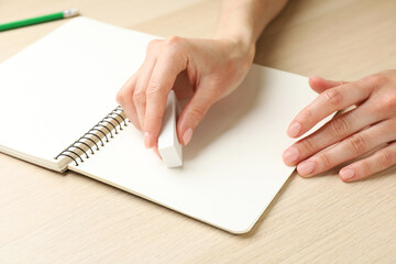 Woman erasing something in notebook at wooden table, closeup