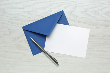 Envelope with blank paper card and pen on white wooden table, flat lay