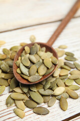 Spoon with pumpkin seeds on white wooden table, closeup
