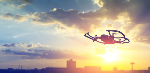 Silhouette drone flying overhead in cloudy sunset city sky.