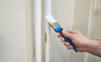 A man's hand paints a battery with a brush in white paint. The concept is an apartment renovation. 