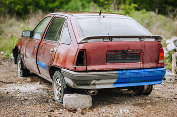 An old, red, broken, discarded car stands in a landfill after the war in Ukraine in nature.