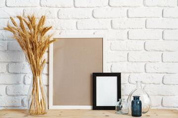 Vase with ears of wheat and photo frames against brick wall