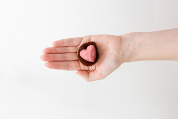 Handmade chocolate sweets above white background. Female hands holding candy pink heart
