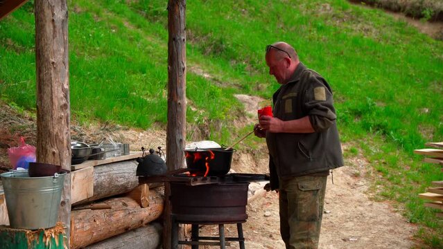 Male hunter prepares food outdoors near fireplace. German wirehaired pointer. Hunter with his shotgun in middle of nature. Bushcraft, hunting and people concept